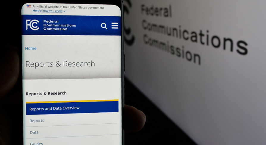 Smartphone displaying the Federal Communications Commission website on the “Reports & Research” page, with a blurred FCC background.